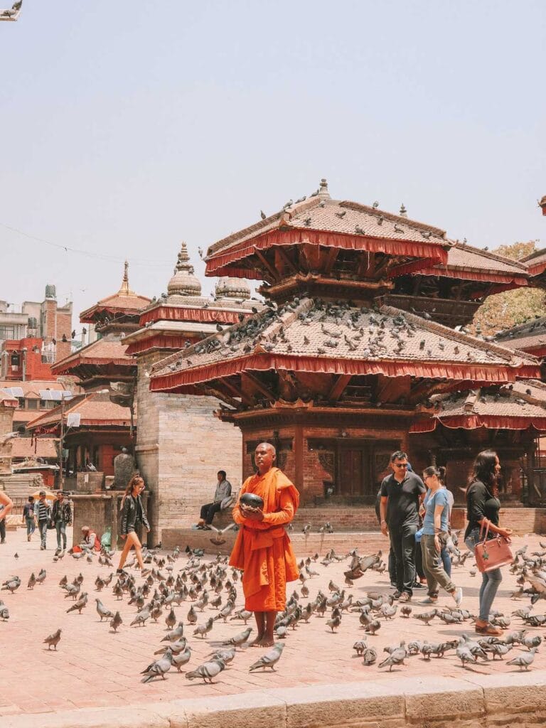 Local monk standing in crowd holding bowl. Surrounded by pigeons at Kathmandu Durbar Square