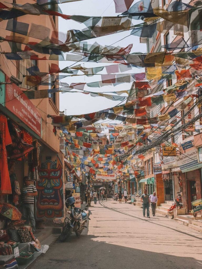 looking down a safe street in Nepal, many colorful prey flags hanging between shops