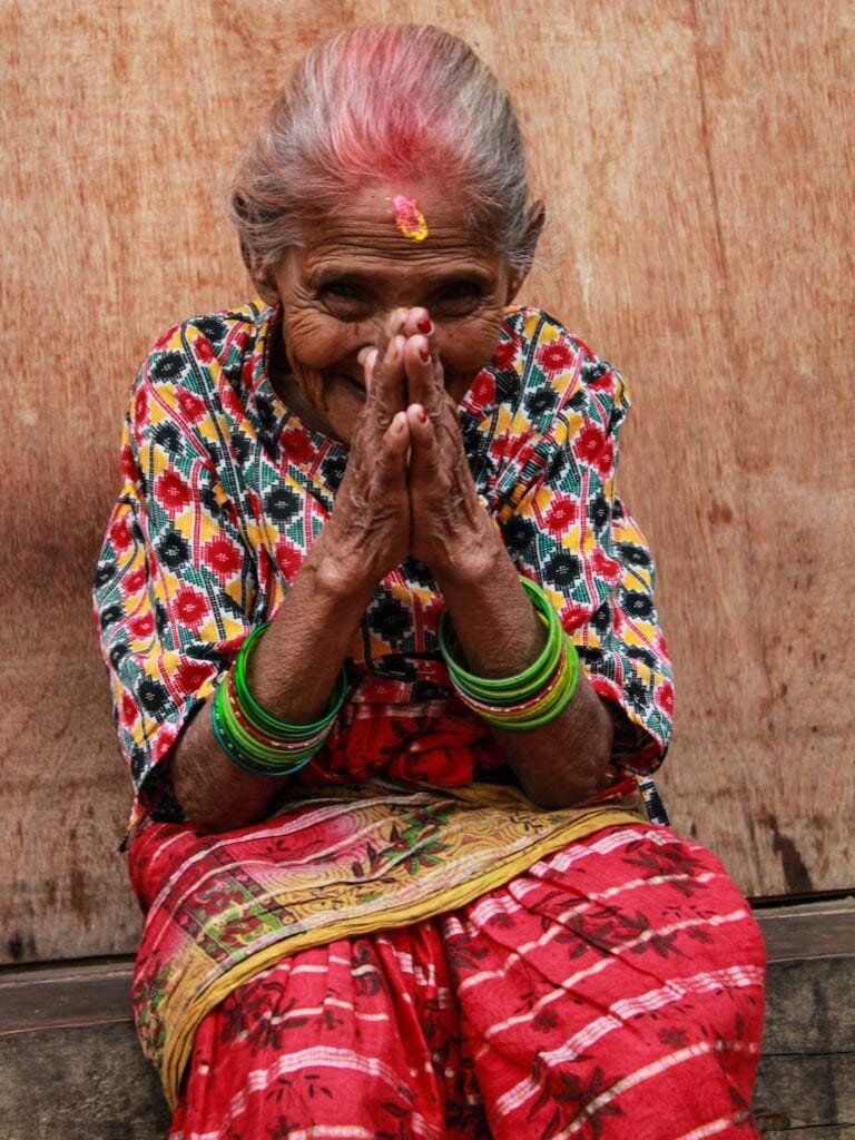 Elderly Nepalese lady wearing bright colors and hands in preying position