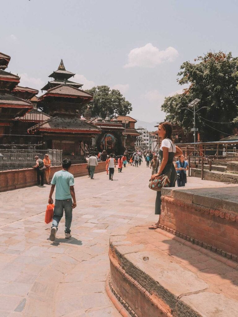 Me standing on brown stone steps, facing temples in durbar square, having a safe time in Nepal