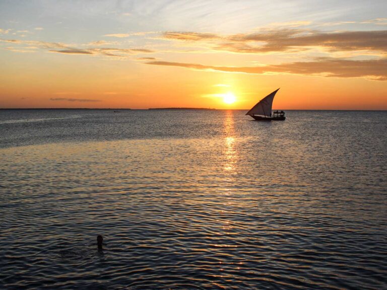 Swimming at Sunset in Zanzibar, towards the horizon a sail boat is close to passing the sun going down