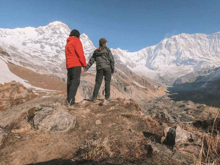 Husband and wife standing, holding hands, looking at snow covered mountains after completion of Annapurna base camp trek.