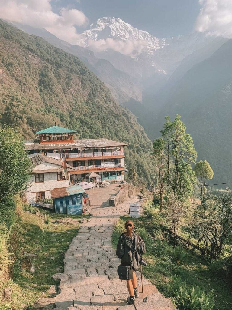 A World To Live walking through a small village while trekking in Nepal. Snowy mountains can be seen in the background.