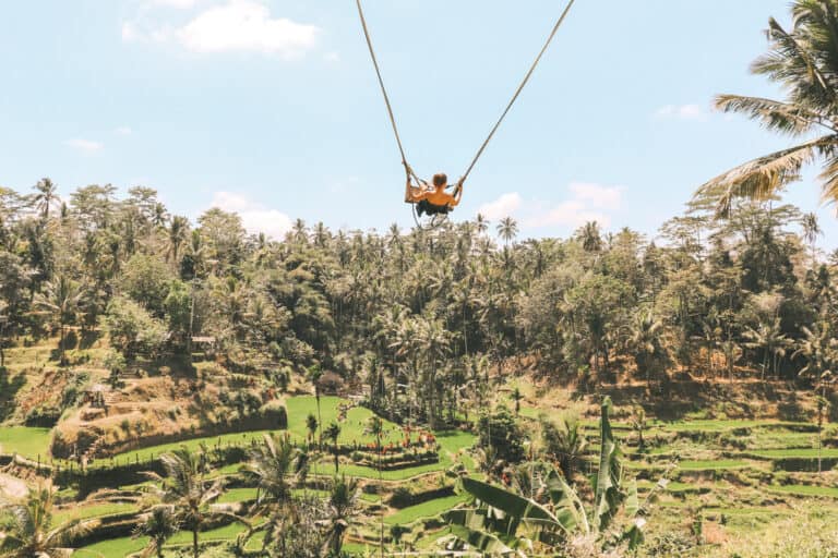 Elyse on a swing while traveling in Bali. She is swung high out over green rice terraces