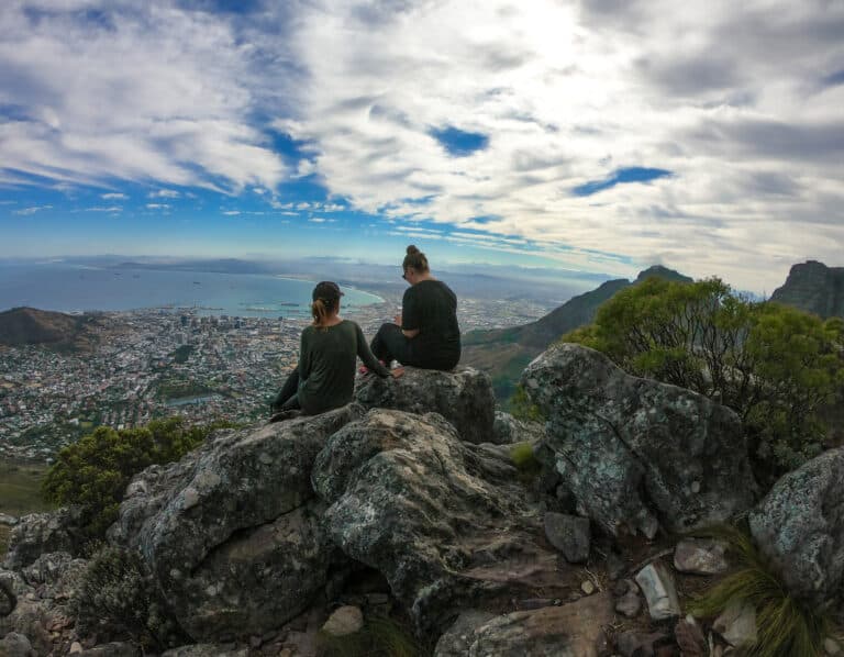two females sitting on large rocks, looking at the view of Cape Town and the Atlantic Ocean