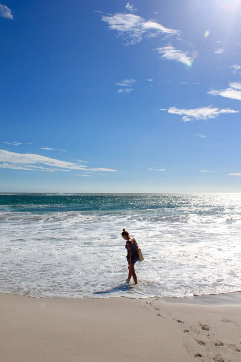 The Atlantic Ocean on a sunny day. Female wearing blue standing in the shallow water while traveling cape town