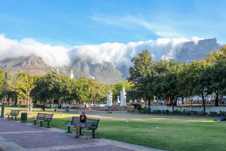Female sitting on bench surrounded by green grass and trees. Large cape town Mountain in the background