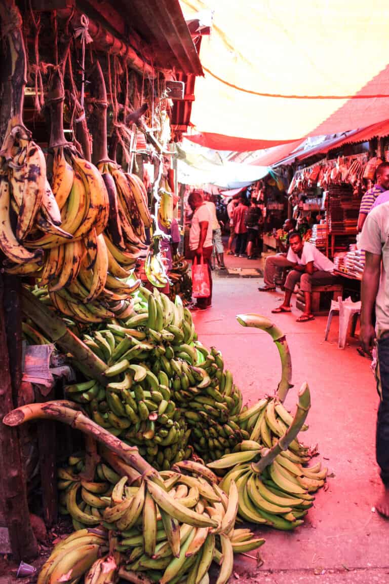 an aisle of a local markets in stone town. A number of large bunches of bananas are leaning up against a bench