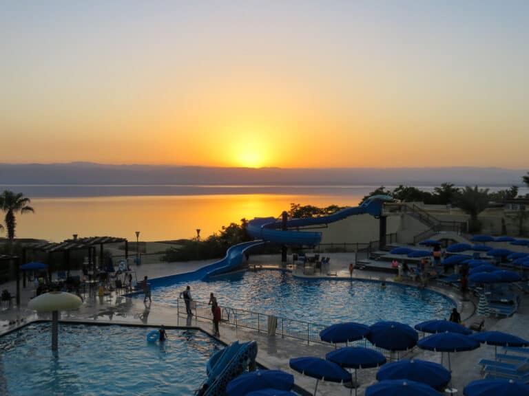 The sunset is bright yellow in the distance and a resort with two pools and a waterslide is the main focus