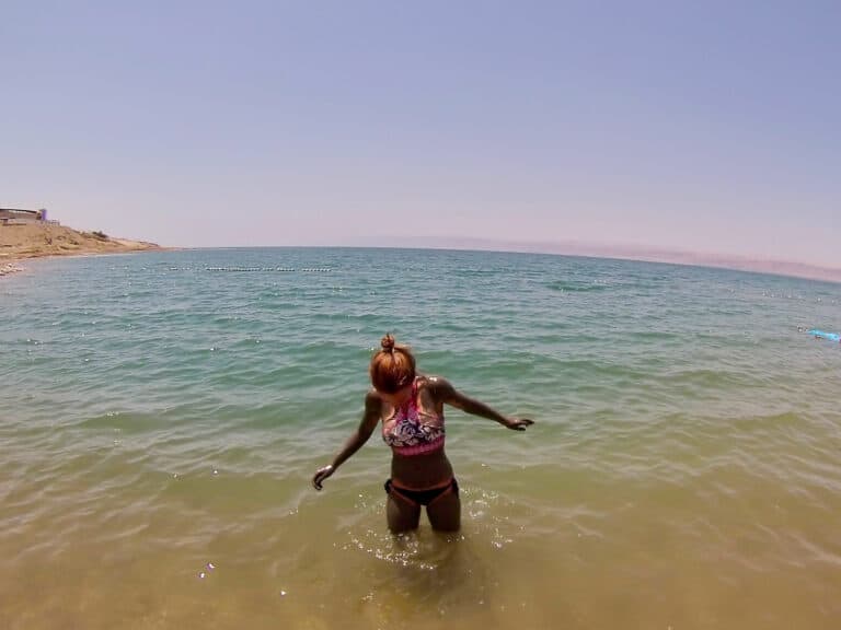 A female stands in the water of the Dead Sea in Jordan, covered in mud looking down at herself.
