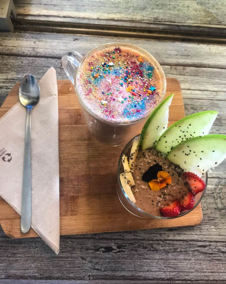 Breakfast served at Nourish'd Cafe. Taken from a high view looking a brown pudding and fruit next to a coffee with colorful glitter on top