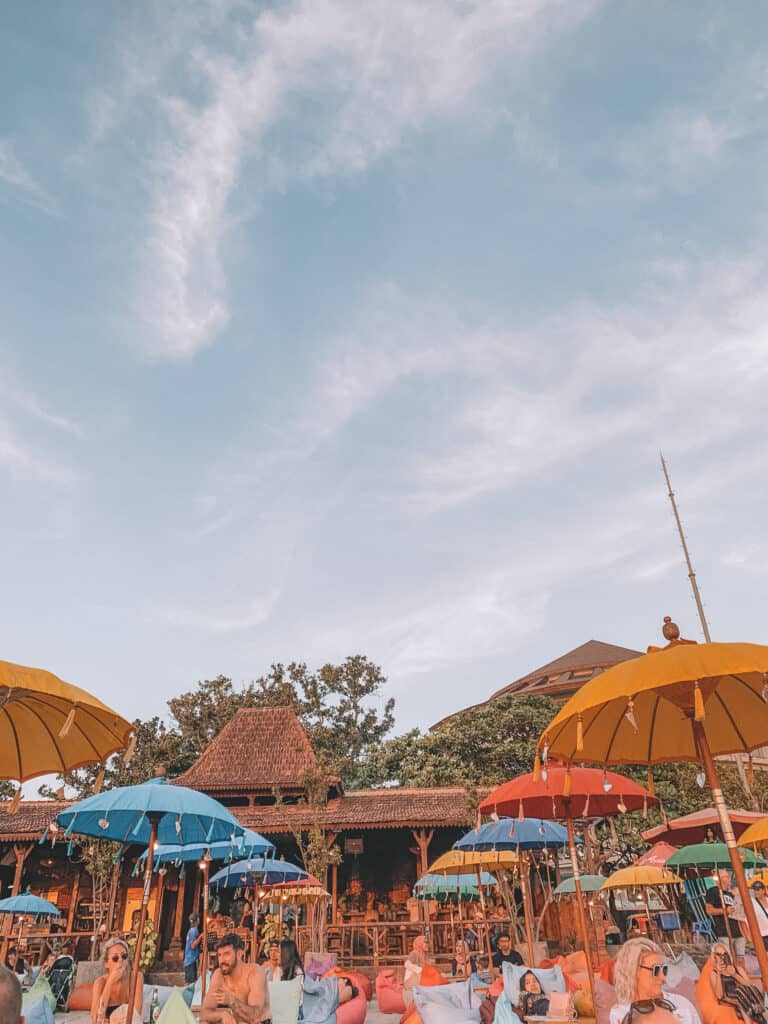 Set up on the beach in Bali, travelers dining at out door restaurant. They are all sitting on beanbags under colorful umbrellas