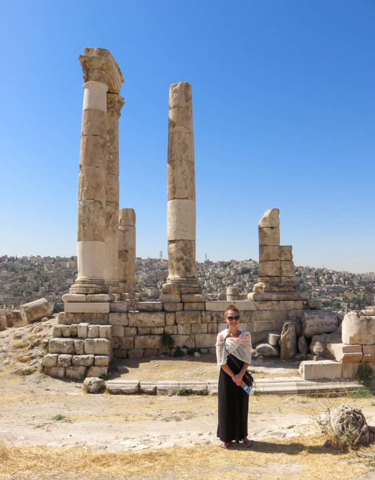 taken while traveling in Jordan, a female stands facing the camera smiling and in the background are tall ruins
