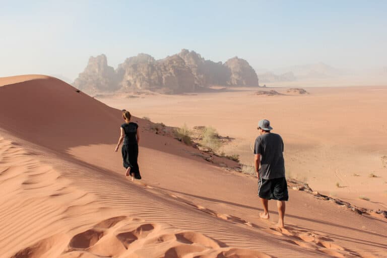 two people who are traveling in Jordan walk across the sand in Wadi Rum Desert