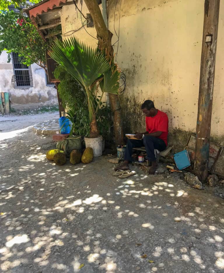 a local painter sits under a tree and in front of a yellow wall