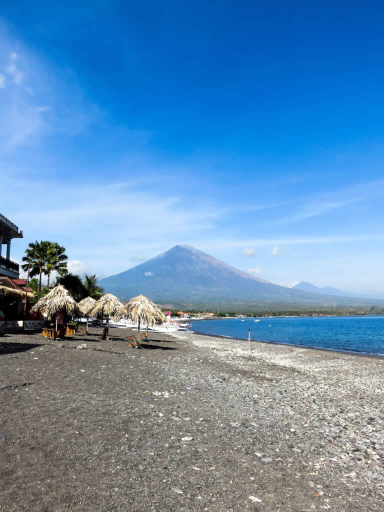 Looking down Amed Beach in Bali, the beach is covered in rocks and Mt Agung is in the distance
