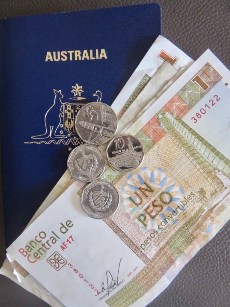 An Australian passport on a leather surface, Cuba money, note and coins, are placed on top.