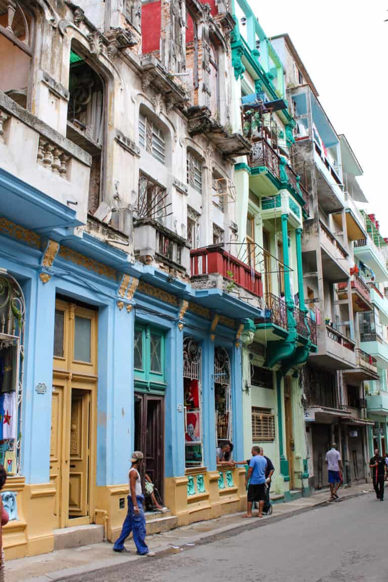 four story buildings line a street. The buildings have small balconies and painted bright colors