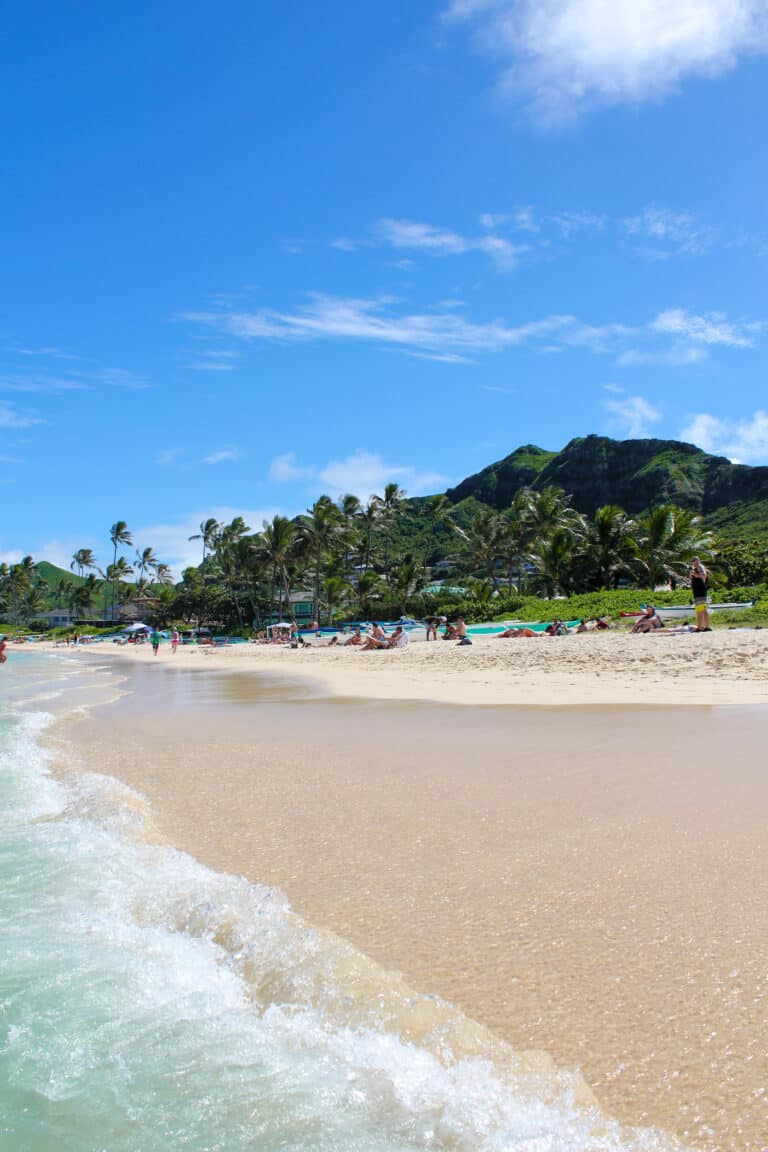 a sunny day at the beach in Hawaii, the waves are rolling in and many people are laying on the sand