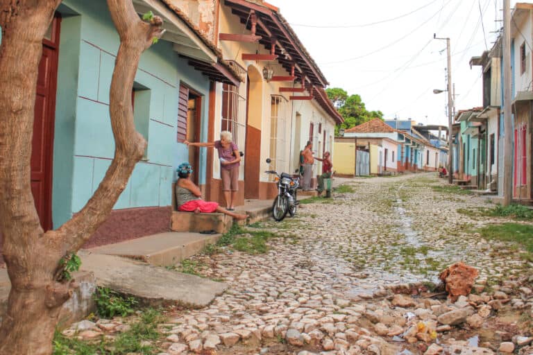 Colorful buildings line the cobble stone streets in Trinidad, local men and women stand outside the buildings talking to each other