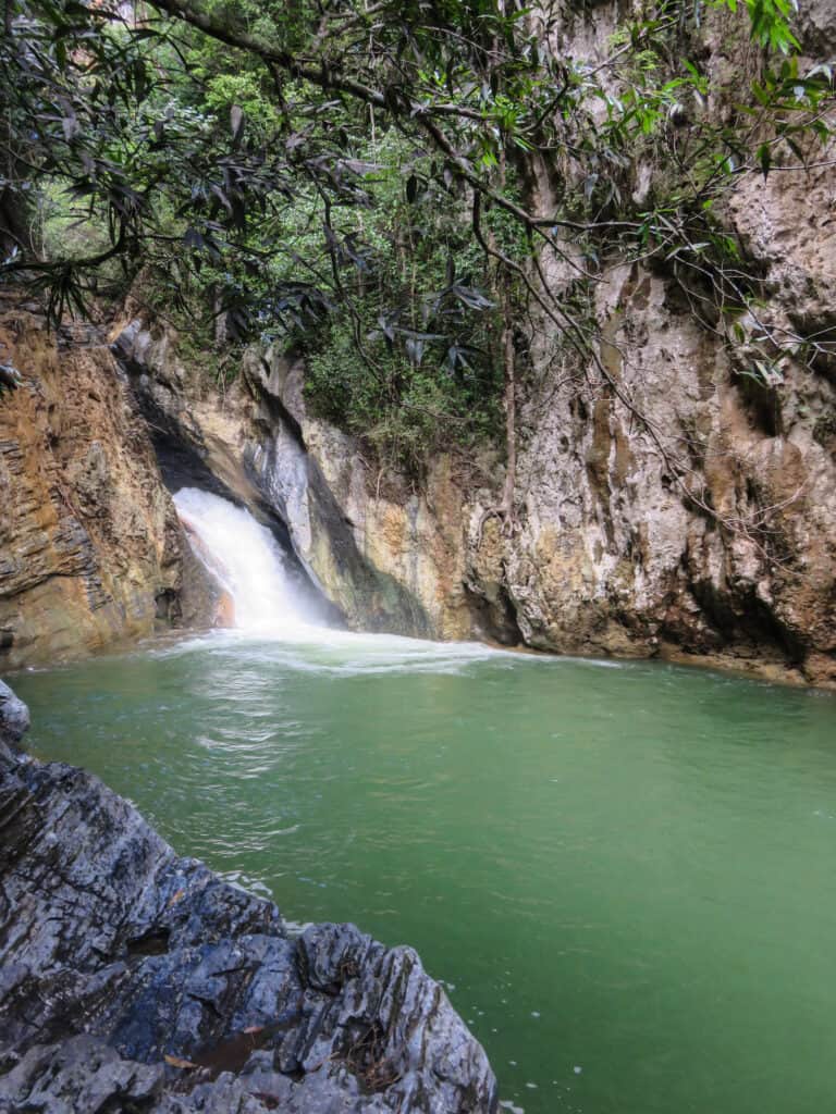 visiting a waterfall in Cuba. small waterfall flows into the green water. cliffs and trees surround the waterfall