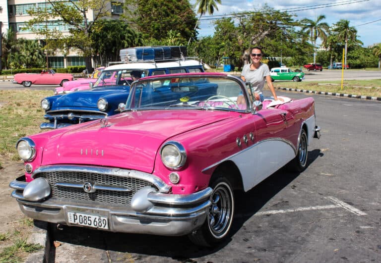 elyse sitting in the back of an old car while visiting Cuba. The car is a hot pink convertible