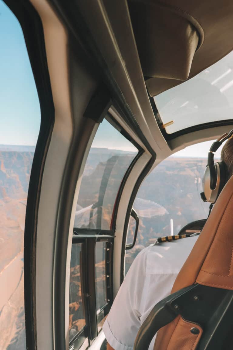 from the back seat of a Helicopter flying over the Grand Canyon. the side of the pilot can be seen
