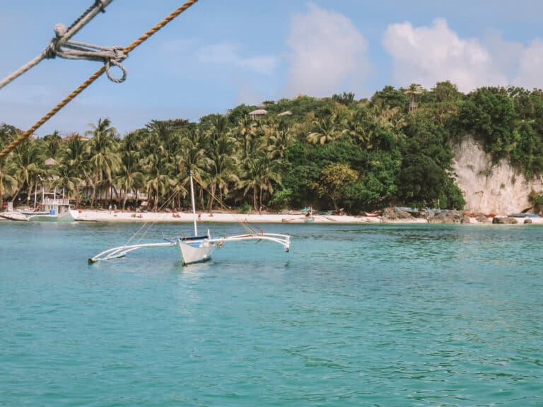 a Sail boats in Boracay, anchored in the ocean. the beach is in the background with palm trees lines the shore