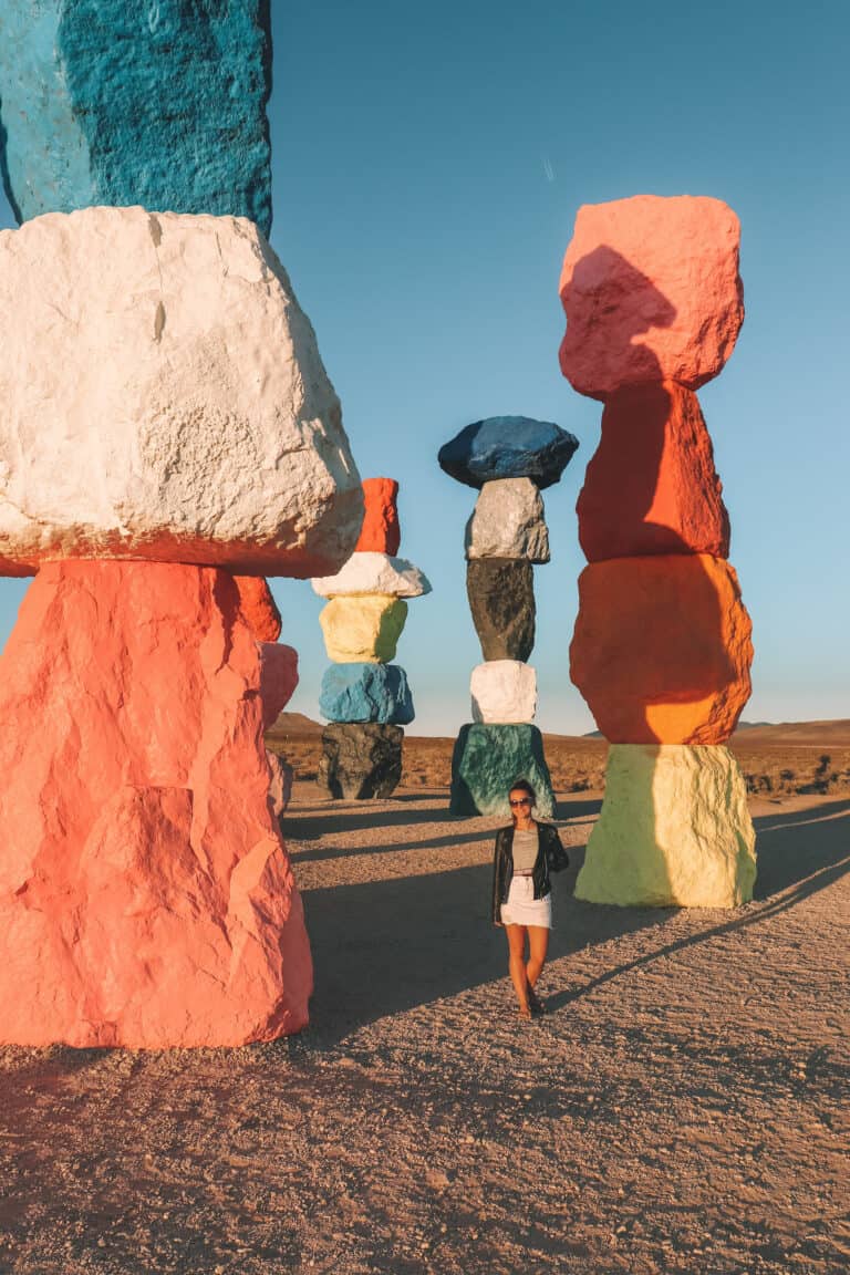 elyse walking in an art installation in the Nevada desert. seven towers of bright colored boulders piled on top of each other surrounding her. During one of the day trips from Las Vegas