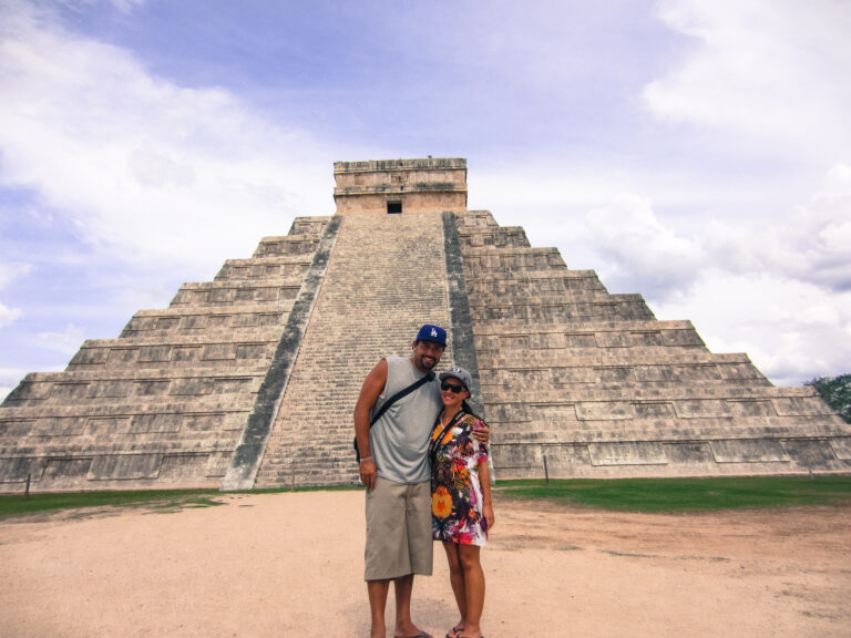 Elyse and Lawrence standing in front of a mayan ruin in the shape of a pyramid. The area doesn’t have others walking around and its a very sunny day.