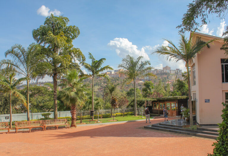 The court yard in front of the Genocide Memorial, the paved ground is lined with wooden benches and tall palm trees.