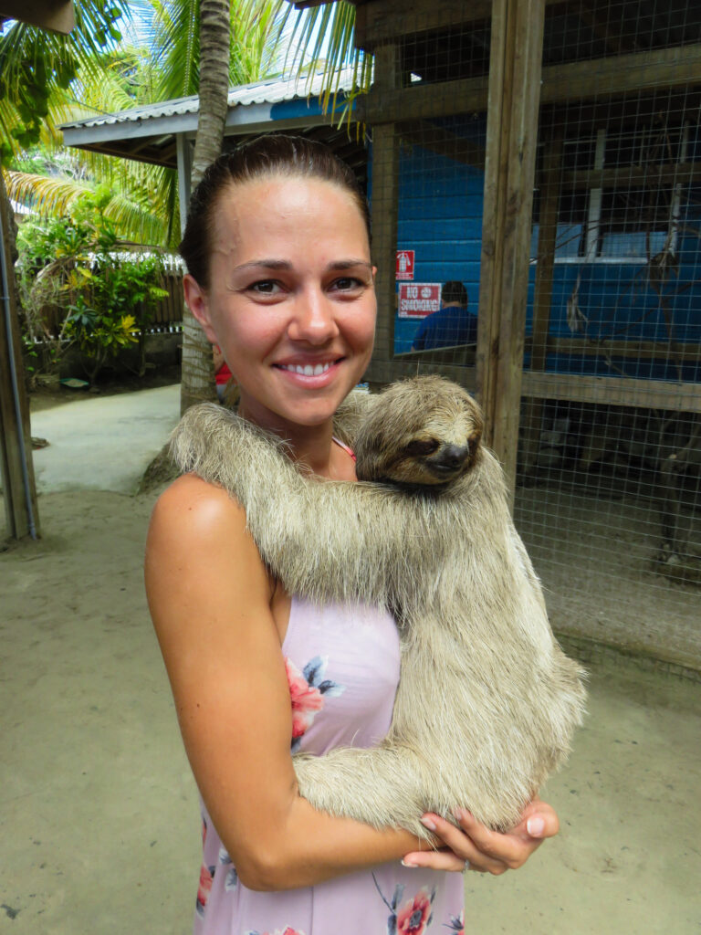 Elyse standing up holding a small sloth, this took place in Roatan