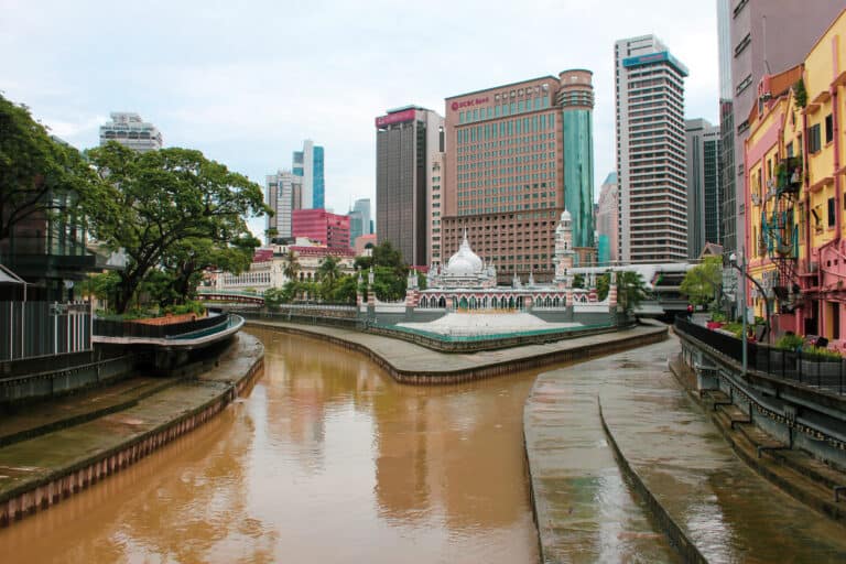 In Kuala Lumpur city a river spilts off in two different directions. Every side of the river is lined with tall buildings and one mosque in the middle