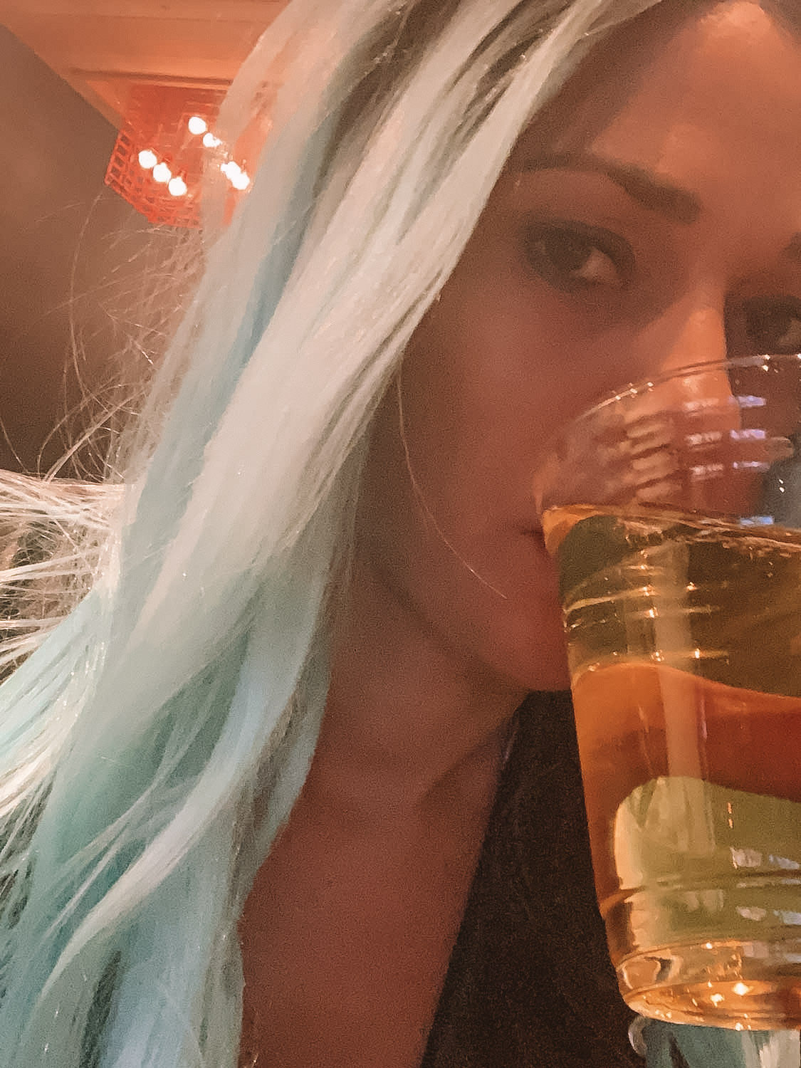 With a devastated look on her face, Elyse drinks a beer with a blue wig on.