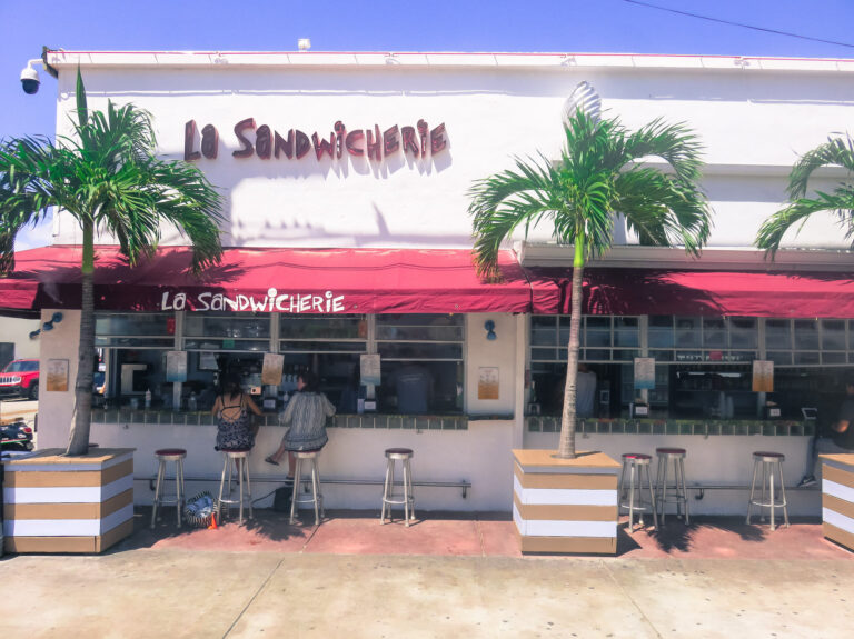 An image of two women sitting at the window of a sandwiched Restaurant in south beach miami. All the other stools along the window are empty.