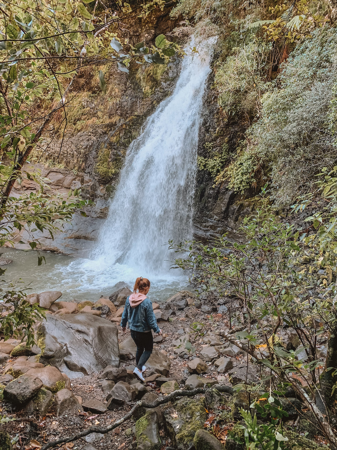 Elyse walking down wet rocks towards a small river. A heavy flowing waterfall is rushing into the river. This was taken in her first month of the year recap