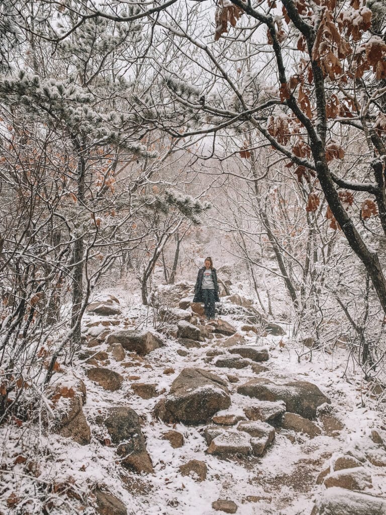Elyse walking down a rocky paths that is covered in snow, during her travel to Seoul