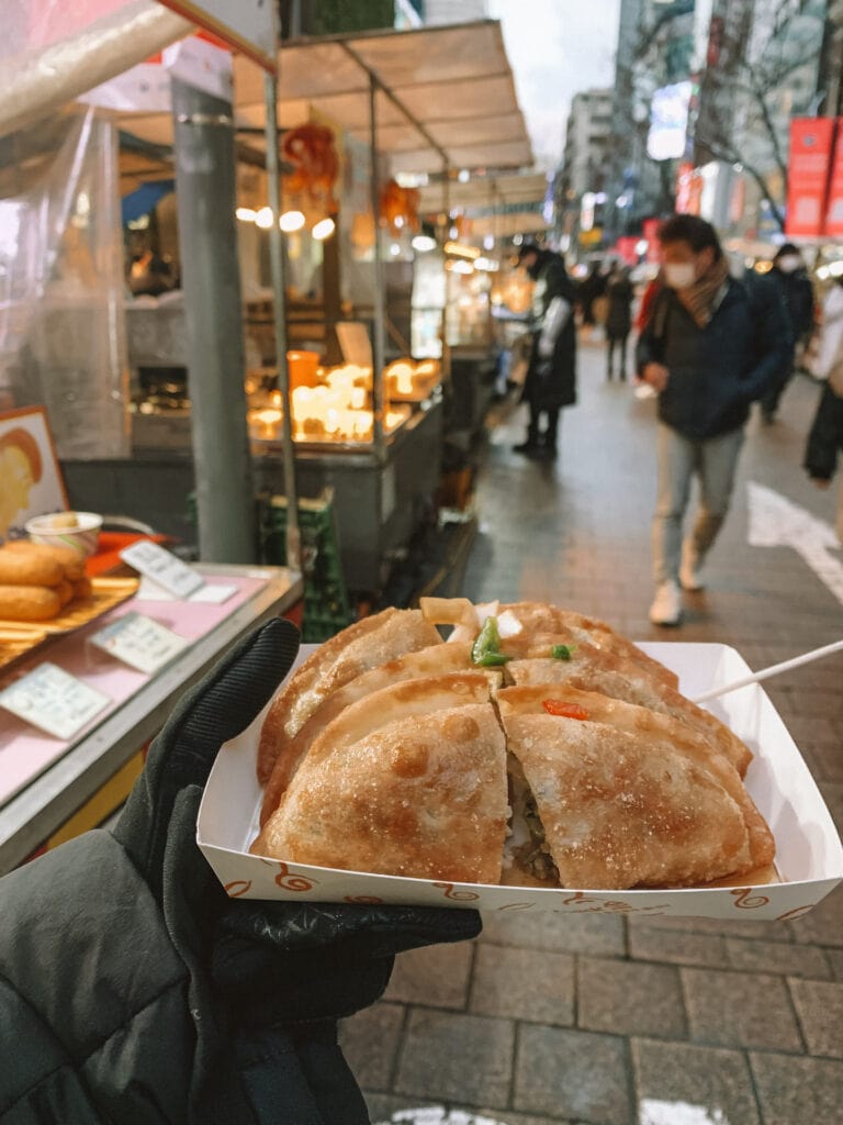 A plate of street food being help up and in the background are both people who travel in Seoul