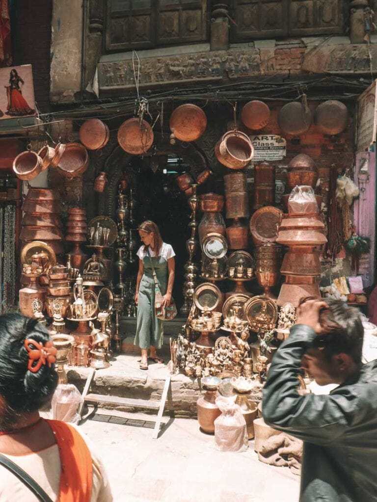 A busy local street in Nepal and Elyse is stepping out of a store selling brass goods.