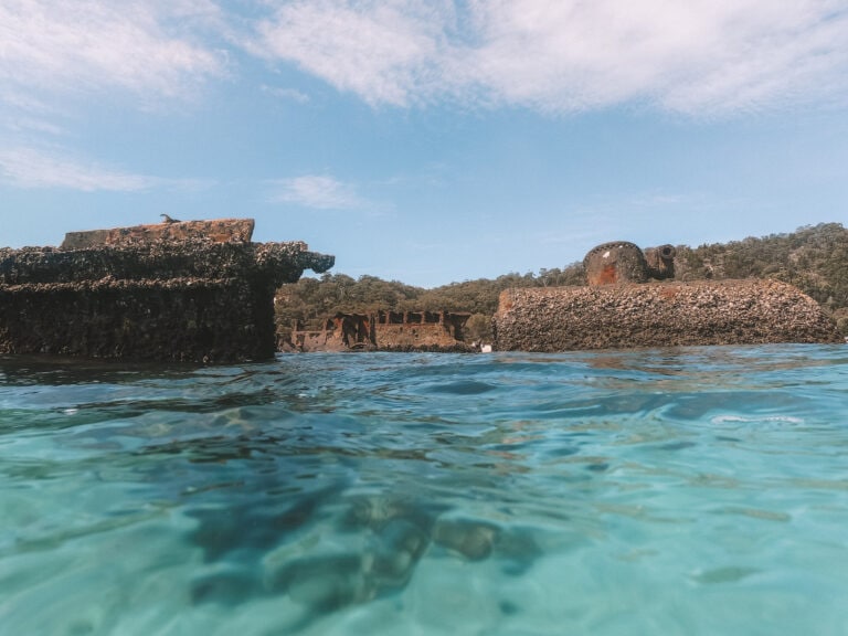 Taken from in the clear blue water at Tangalooma, the side of a shipwreck is sticking out above the water.