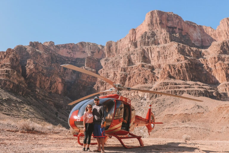 male and female standing in front of a red helicopter and a large rock formation behind them. One of the 14 best travel experiences