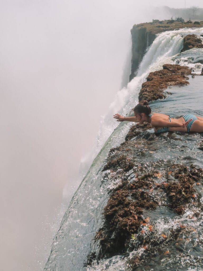 Elyse laying in a pool of water in her bather, she right at the top of a waterfall looking over the edge. One of my best travel experiences