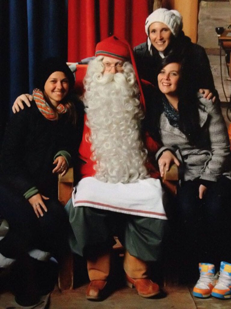 Three females sitting next to a man dressed as Santa clause. He has a red hat and a long curly beard