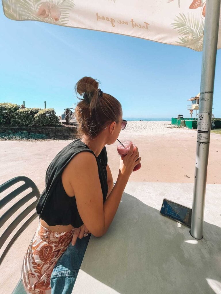 Elyse drinking a juice on the sunny Gold Coast day. The cafe is in Broadbeach and the blue ocean is in the distance