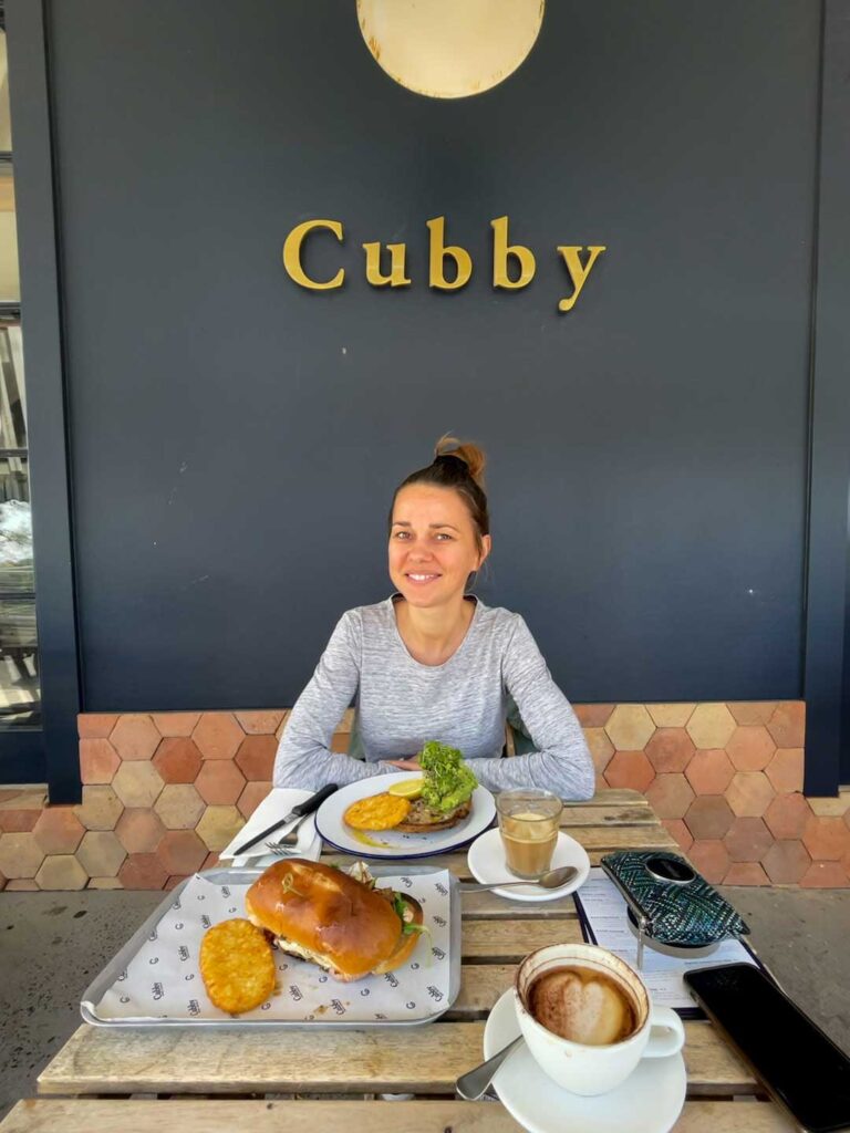 Elyse sitting at a table at cubby back house in the tweed valley. There are two breakfast meals on the table