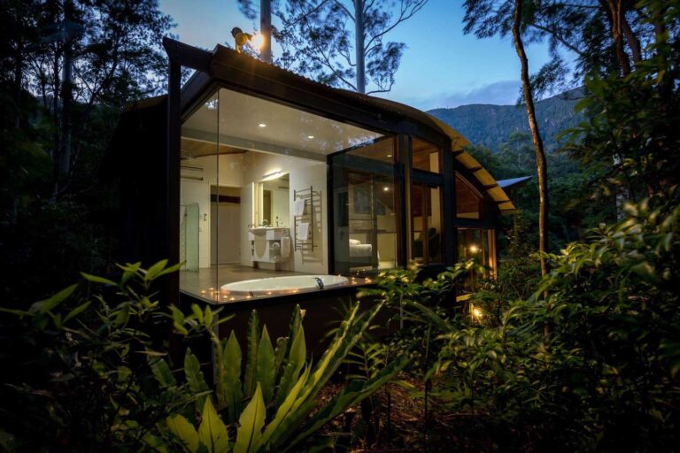 Crystal Creek rainforest retreat in Northern NSW, a romantic getaway perfect for couples. This image is taking in the late evening looking into one of the rooms, through the glass window with the bathroom lit up