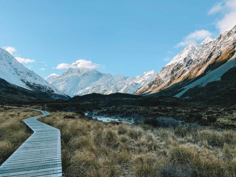 day hiking in New Zealand along the hooker valley track. A wooden path leading towards Mount cook and other snowy mountains. List for packing for a day hike
