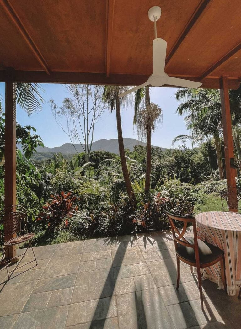 an airbnb that would be a romantic getaway in Northern NSW. There is a table and chair on the front patio and the view is of the rain forest and mountains on a sunny day