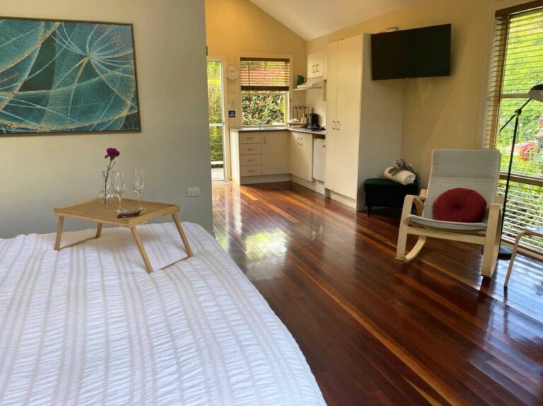 inside the cabin at Tambourine Gardens accommodation. At the end of the bed there is a wooden tray with a rose and two wine glasses