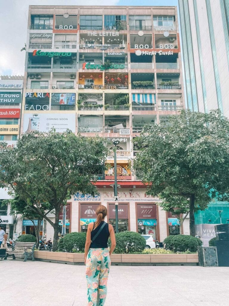 Elyse standing in front of an old apartment building in Ho Chi Minh City, that is now different cafes and bars